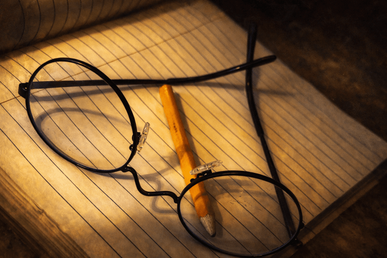 Chapters of My Life visual featuring a pencil and round glasses resting on an open lined notebook, symbolizing revision, reflection, and personal growth.