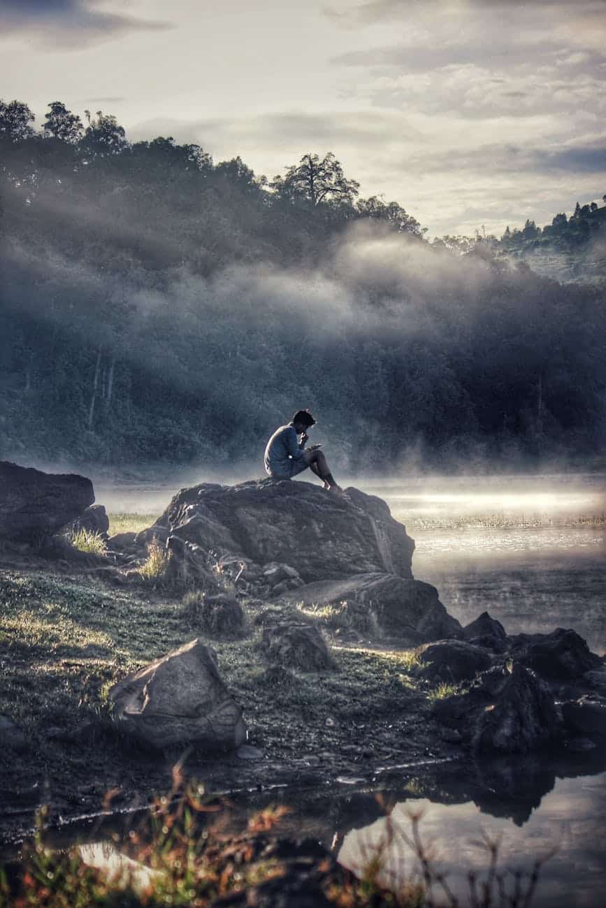 man in gray shit sitting on rock boulder