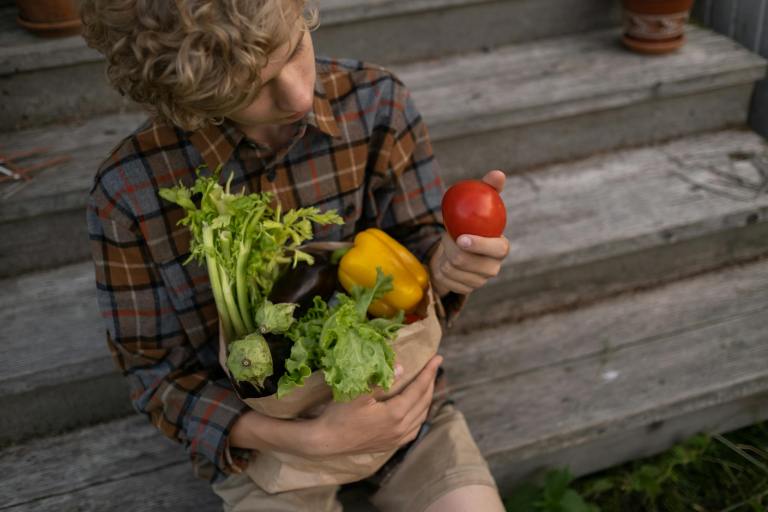 teenage boy holding groceries and looking at tomato